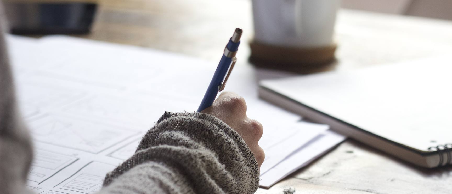 Hand sketching website wireframes on paper at a wooden desk